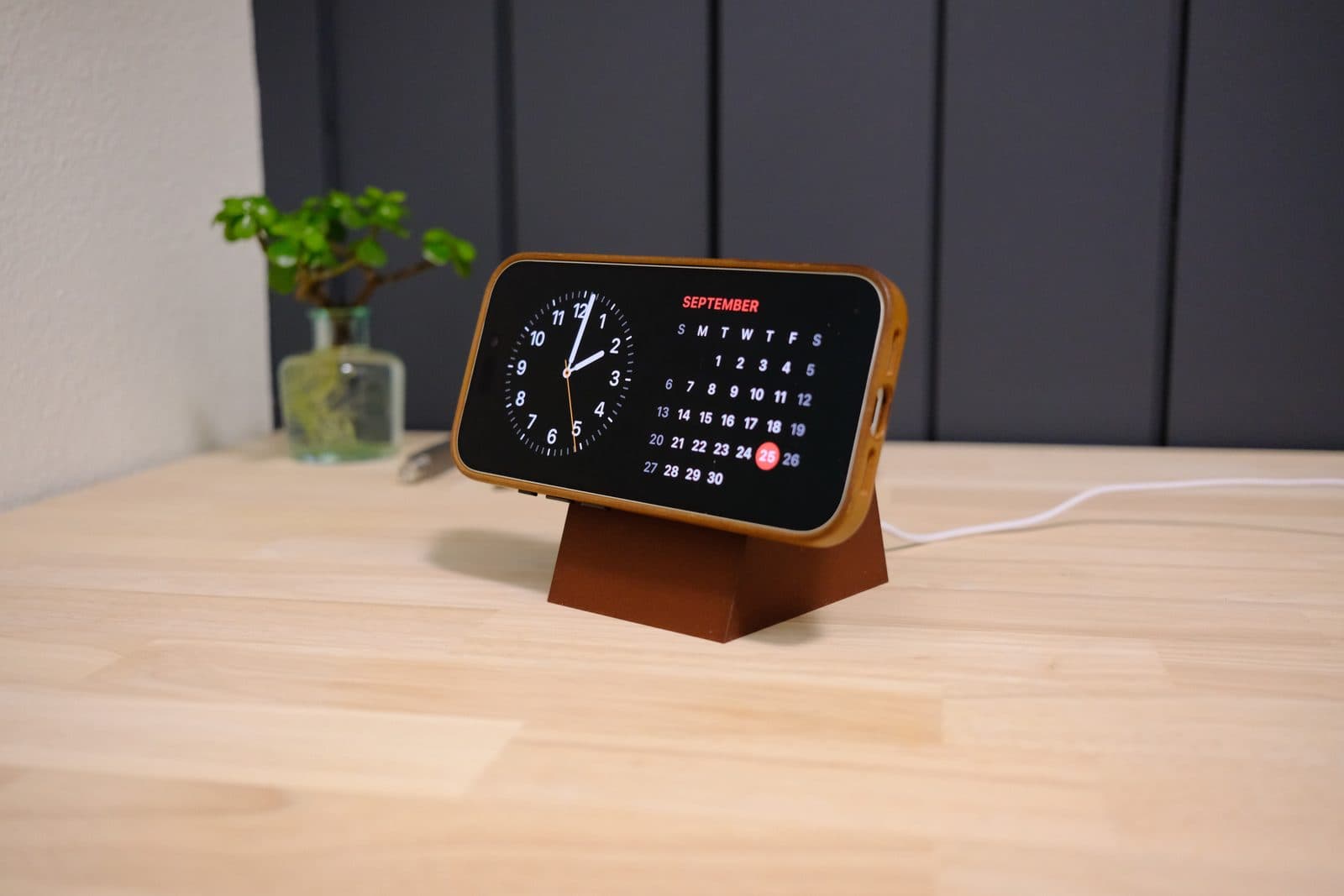 An iPhone in StandBy mode showing a clock and calendar while charging on a brown Dock Block